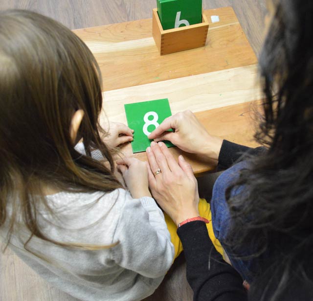 A teacher and a student holding green counting cards with #8 on the card